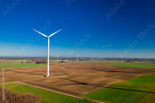 Big white wind turbines in a brown fieldand blue sky