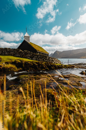 The small picturesque black wooden church of Funningur (Funnings Kirkja) during a sunny spring day with dramatic clouds (Faroe Islands, Denmark, Europe)