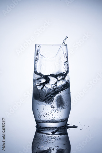 Glass of mineral sparkling water with ice on blue background