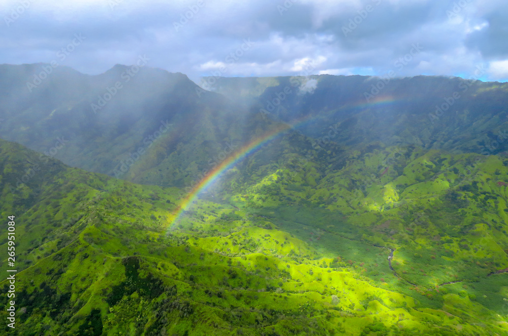 Rainbow over green valley and mountains, panorama shot from a helicopter at Na Pali Coast State Wilderness Park, Kauai, Hawaii, USA Rainbow over green valley and mountains, panorama shot from a helicopter at Na Pali Coast State Wilderness Park, Kauai, Hawaii, USA