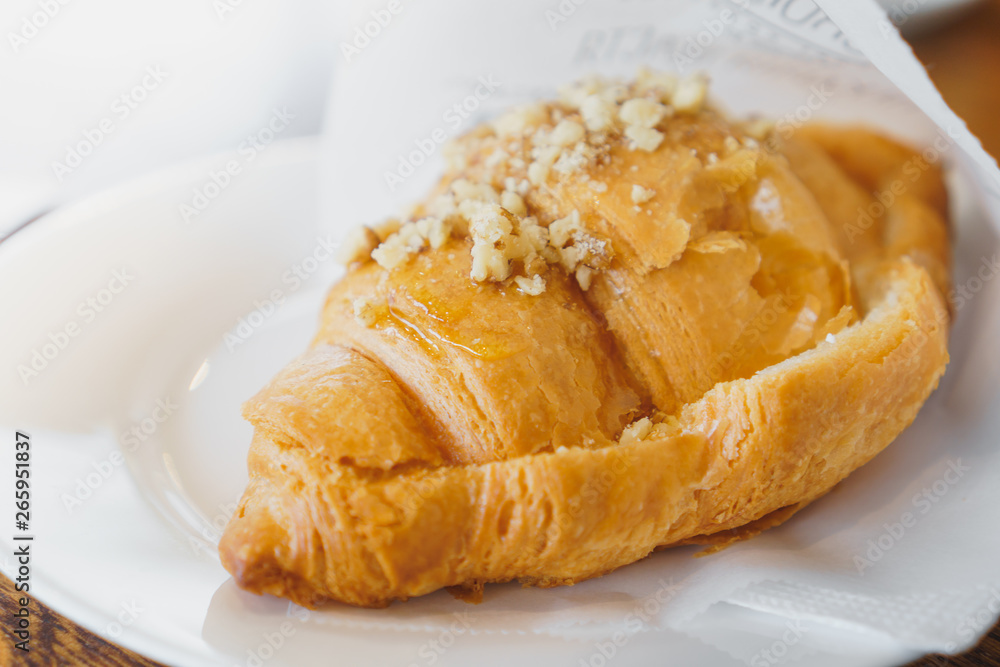 Sweet fresh croissant with honey and nuts on white plate Sweet fresh croissant with honey and nuts on white plate