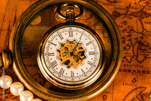 Antique clock in the background of a magnifying glass and books. Vintage style. 1565 old map of the year.