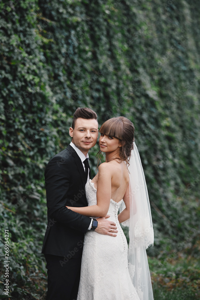 Romantic happy couple newlyweds, bride and groom stands and holding bouquet of pink and purple flowers and greens, greenery with ribbon in the garden. Wedding ceremony on nature. Romantic happy couple newlyweds, bride and groom stands and holding bouquet of pink and purple flowers and greens, greenery with ribbon in the garden. Wedding ceremony on nature.