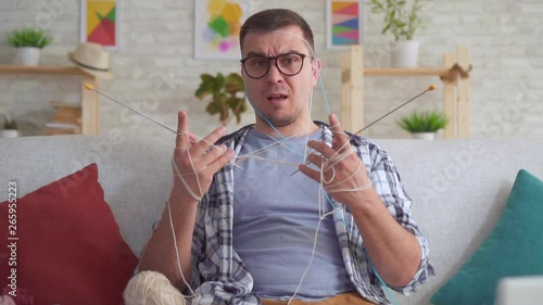 Clumsy young man with glasses knitting needles slow mo photo