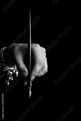 female hand elegantly holding an ink pen with a metal tip close-up on a black background. classic fountain pen isolated macro black and white. copy space. vertical