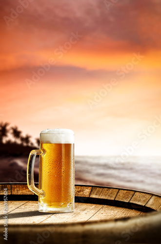 Cold fresh beer on barrel of wood. Summer sunset time. Sea landscape with beach and palms. Free space for your bottle. 