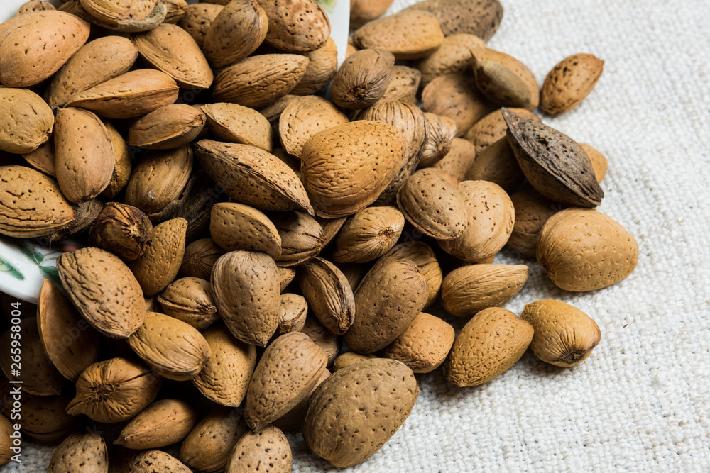Obraz premium Almond nut in shell heap on beige fabric texture