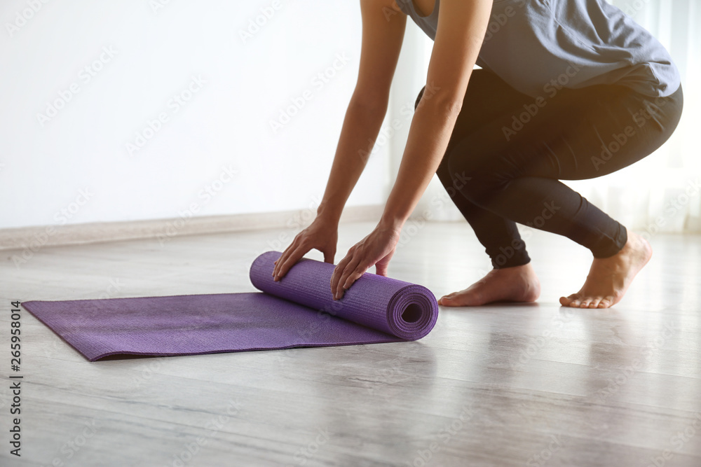 Woman rolling yoga mat on floor indoors, closeup Woman rolling yoga mat on floor indoors, closeup