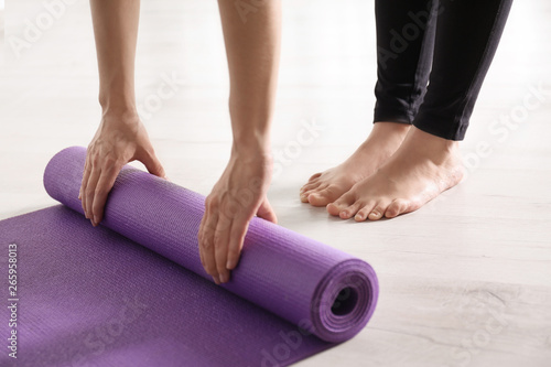 Woman rolling yoga mat on floor indoors, closeup