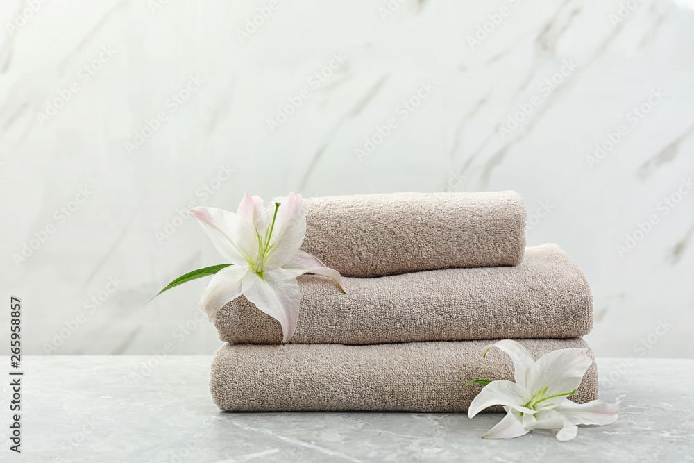 Stack of fresh towels with flowers on grey table against light background Stack of fresh towels with flowers on grey table against light background