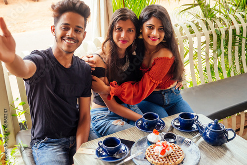 fashionable indian friends couple of two woman and man making selfie mobile phone.friends long-awaited meeting students eating pancake drinking masala tea after shopping.summer instahram lifestyle photo