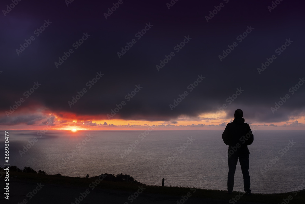 backlit man with orange sun in the background, after bad weather with dark clouds