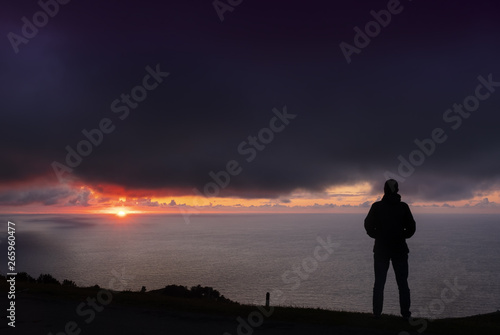 backlit man with orange sun in the background, after bad weather with dark clouds