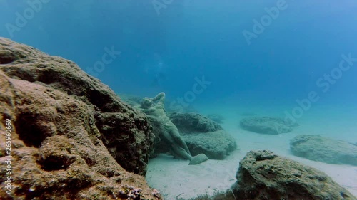 Underwater scene with the statue on the bottom of the sea and several divers floating at the distance