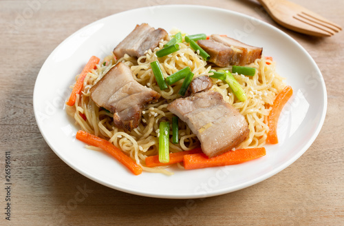 close up of stir fried egg noodles with pork belly in a ceramic dish on wooden table. asian homemade style food concept.