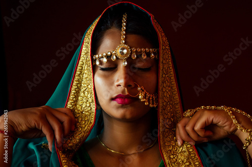 portrait indian beautiful female in golden rich jewelery and tradition saree face closeup professional make-up wearing bindi on head .Muslim Woman face portrait with bindis maang tikka ,nath,nose Pin photo