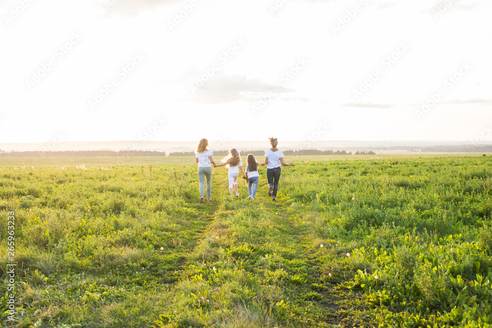 Family, summer and holiday concept - Group of women and girls going away in green field Family, summer and holiday concept - Group of women and girls going away in green field