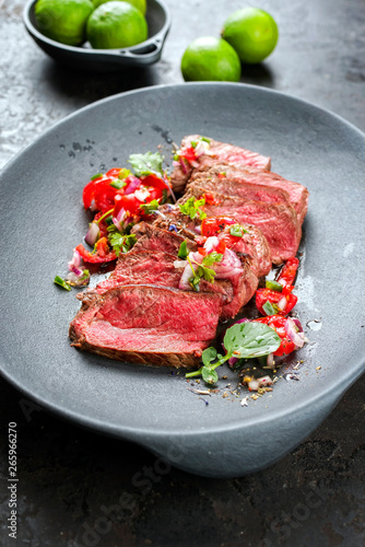 Traditional South American barbecue wagyu roast beef sliced with pico de gallo and salsa verde garnished as top view in a modern design plate