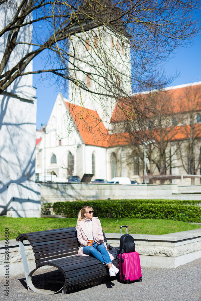 Obraz premium summer travel and vacation concept - young woman sitting with suitcase in old town of Tallinn, Estonia