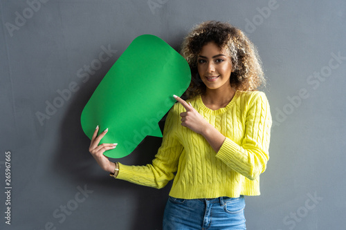 Portrait of a happy young african woman holding empty speech bubble isolated over gray background.
