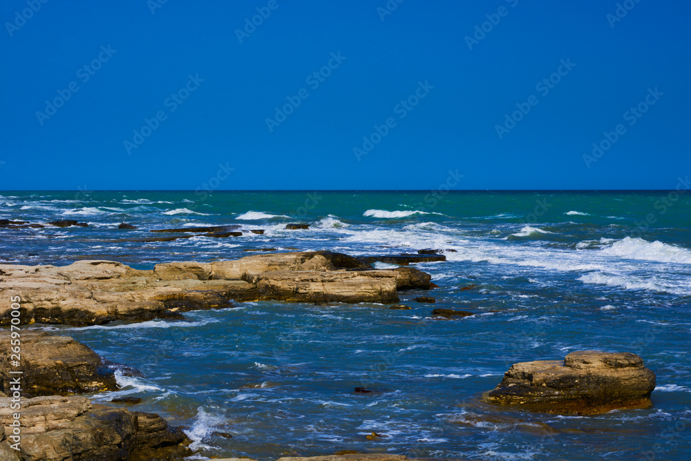Rocky coastline with a cove and rock underwater, split view above water surface, Mediterranean sea, Spain. Azure sea, wave and blue sky. Seascape with sea horizon and clear deep blue sky.