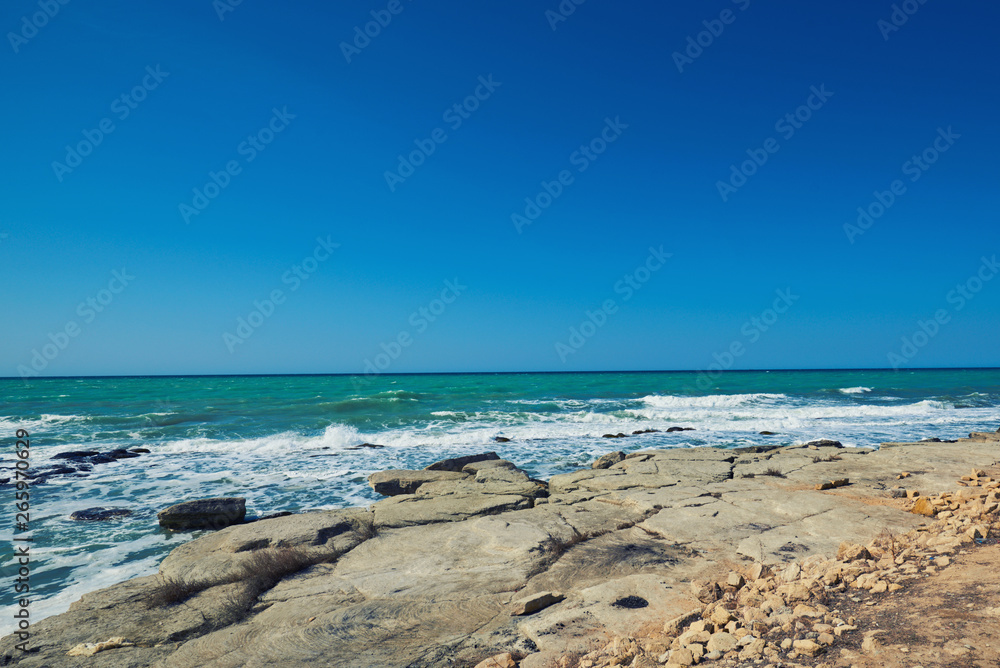 Summer landscape. Rocky coastline with a cove and rock, split view above water surface, Mediterranean sea, Spain. Azure sea, wave and blue sky. Seascape with sea horizon and clear deep blue sky.
