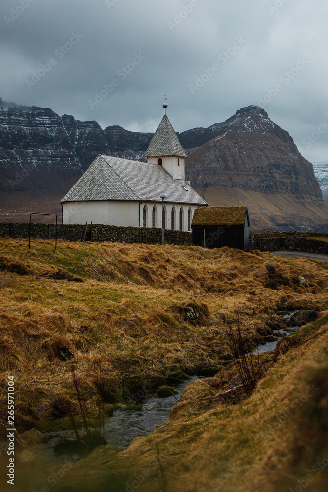 View onto the church of Viðareiði (Viðareiði Kirkja) with moody cloudy sky, fog and snow-covered mountains (Faroe Islands, Denmark, Europe)