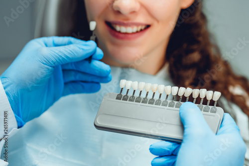 Dentist selecting patient's teeth color with palette in clinic, close up view.