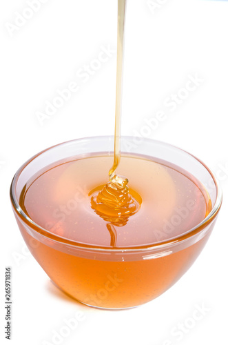 Pouring honey into a glass bowl on a white background
