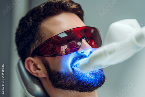 Teeth whitening. Man having teeth whitened by dental UV laser whitening device. Teeth whitening machine,eyes protected with glasses.