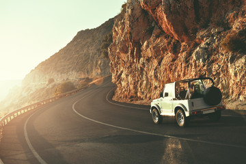 SUV car driving along empty country road at golden summer sunset. People traveling, road trip on lycian way through beautiful mountains coast scenery in sunny summer. Happy journey concept