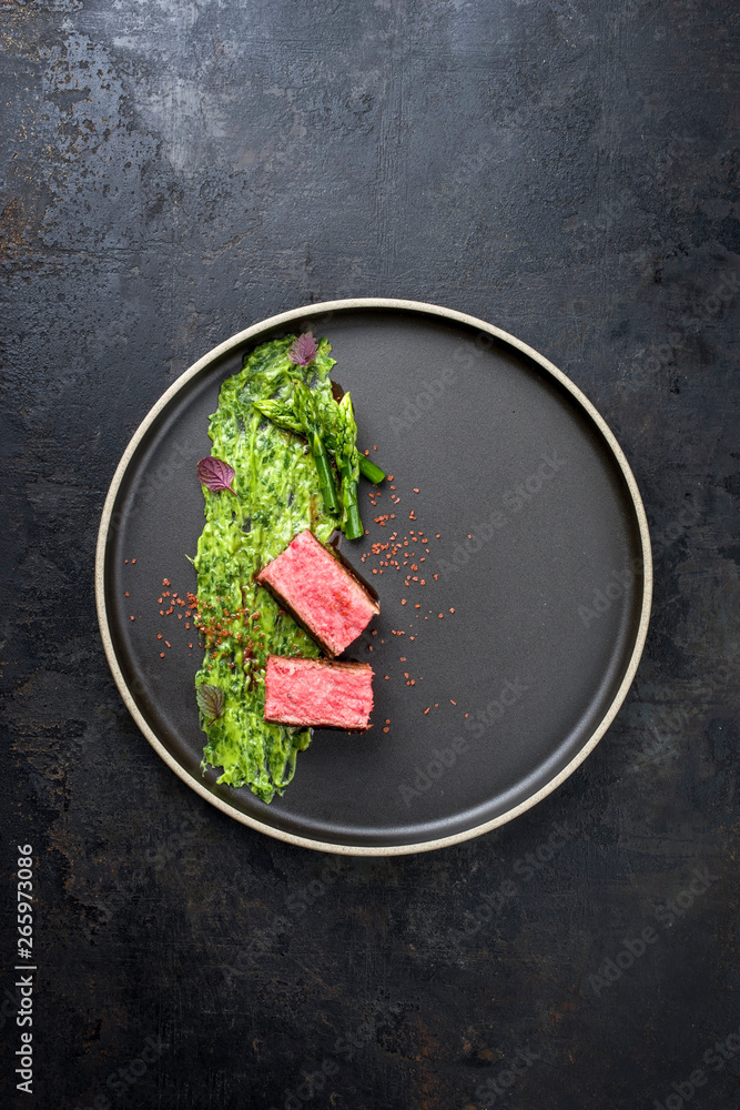 Blanched green asparagus tips with barbecue dry aged wagyu fillet steak and avocado coriander relish as top view on a modern design plate with copy space Blanched green asparagus tips with barbecue dry aged wagyu fillet steak and avocado coriander relish as top view on a modern design plate with copy space