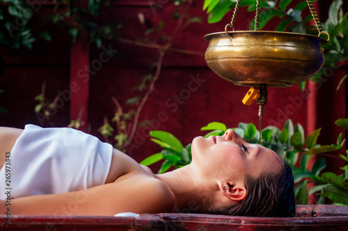 ayurveda massage alternative healing therapy.beautiful caucasian female getting shirodhara treatment lying on a wooden table in India salon photo