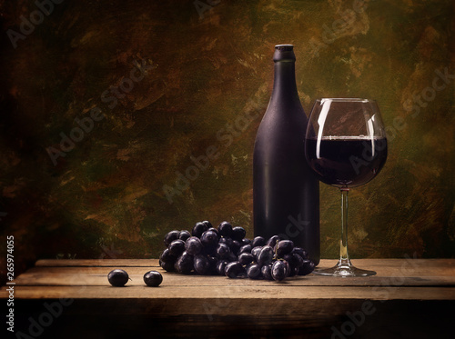 Still life, grapes, a glass of wine, a dark bottle, on a motley, brown background, on a wooden table top made of natural old boards