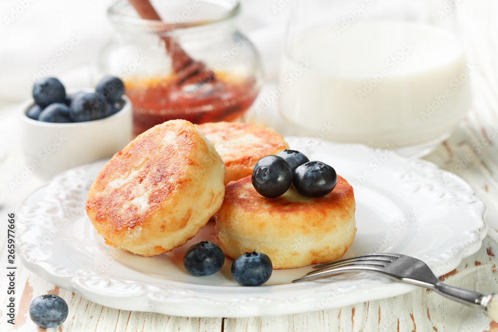 Cottage cheese pancakes, syrniki, curd fritters with fresh berries blueberry and honey in a white plate. Gourmet Breakfast. Selective focus