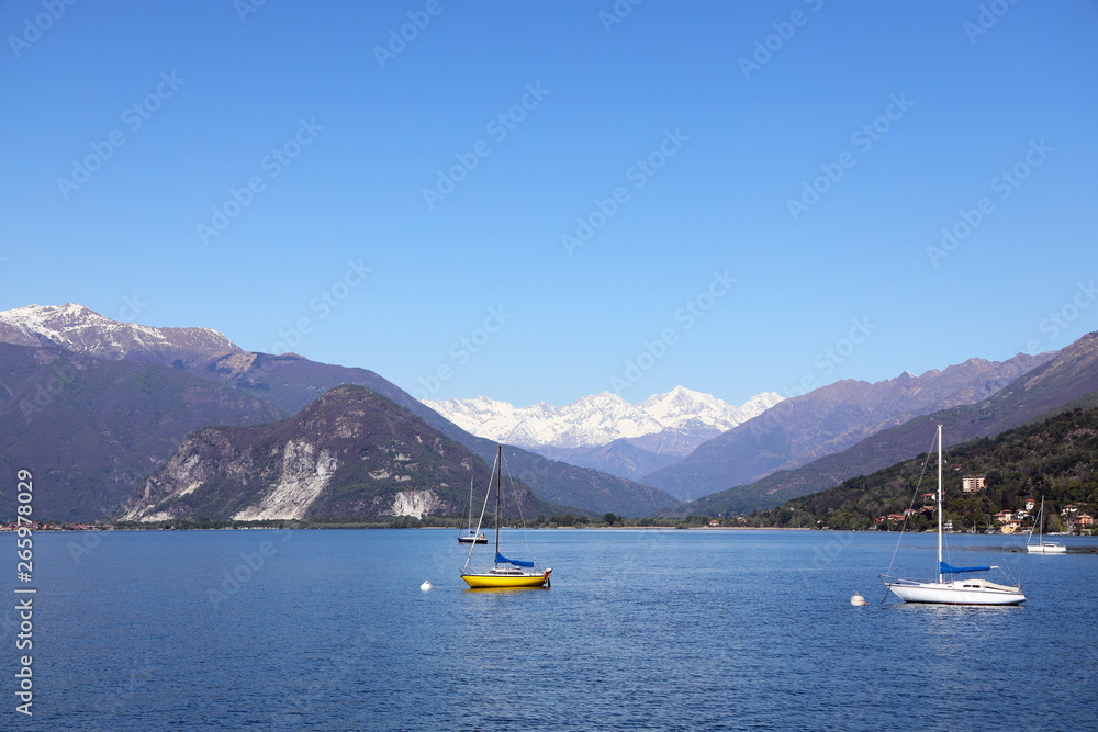 Maggiore lake with sailing boats panoramic view. Piedmont Italy Europe. Lake with sailing boats and view of snow rocky massif at spring or summer time. Travel and vacation concept.- Image