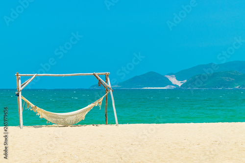Wooden hammock on beach with yellow sand and green island background
