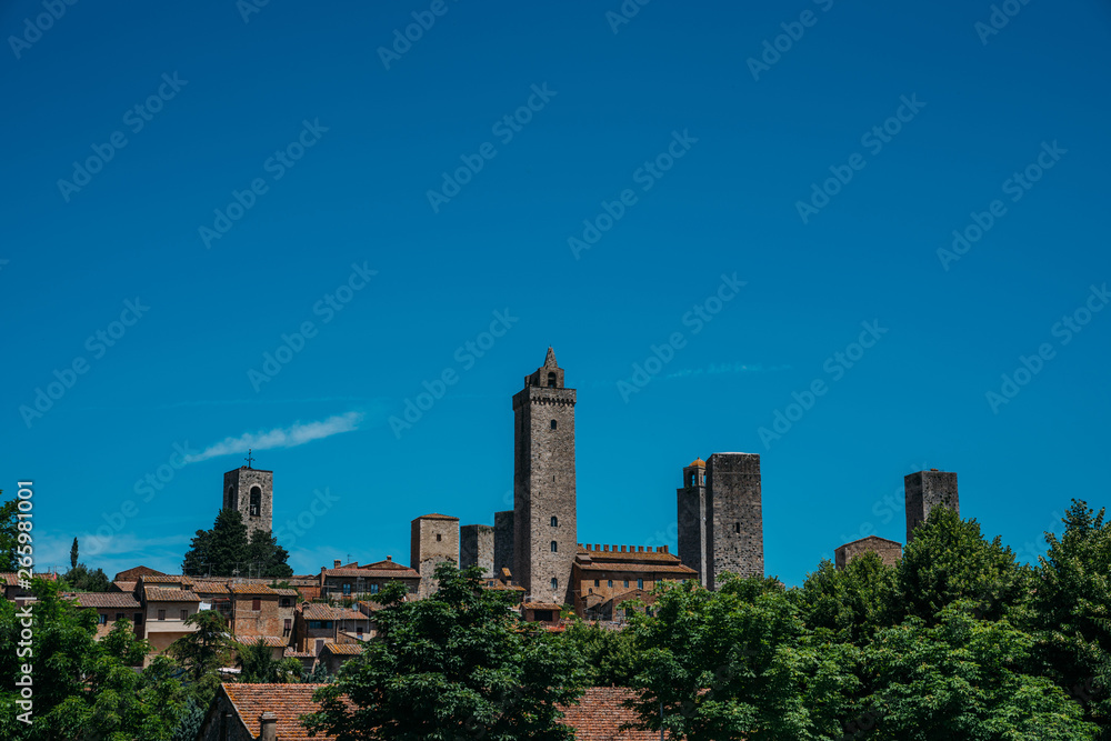 San Gimignano town skyline and medieval towers on tne sky background. Trees in foreground. Tuscany, Italy, Europe. Summer, holiday, traveling concept.
