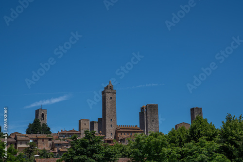 San Gimignano town skyline and medieval towers on tne sky background. Trees in foreground. Tuscany, Italy, Europe. Summer, holiday, traveling concept.