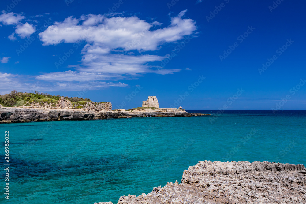 Archaeological site and tourist resort of Roca Vecchia, Puglia, Salento, Italy. Turquoise sea, clear blue sky, rocks, sun, in summer. The sixteenth-century lookout tower. White clouds and strong wind.