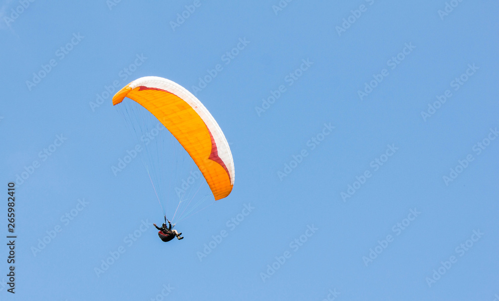 Paraglider waving his hand at the camera on an orange parachute on a bright day against a blue cloudless sky. Active lifestyle, extreme, healthy way to live. Paraglider waving his hand at the camera on an orange parachute on a bright day against a blue cloudless sky. Active lifestyle, extreme, healthy way to live.
