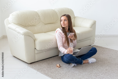 Technologies, freelance and people concept - young woman working at home, she is drinking water on the floor, chatting in laptop