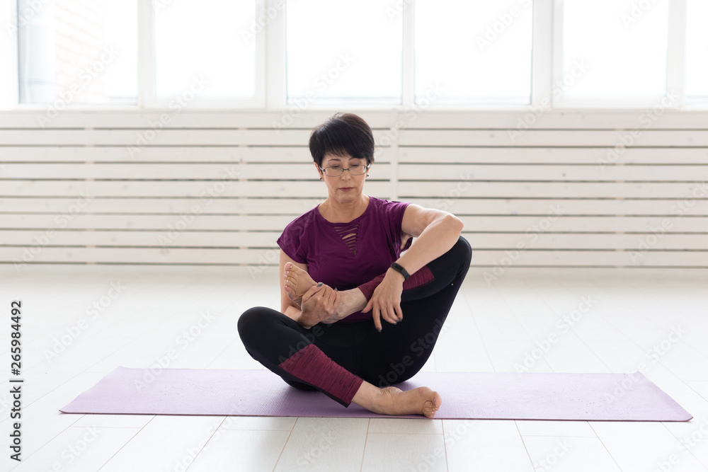 People, yoga, sport and healthcare concept - Attractive middle-aged woman stretching and sitting in yoga lotus position People, yoga, sport and healthcare concept - Attractive middle-aged woman stretching and sitting in yoga lotus position