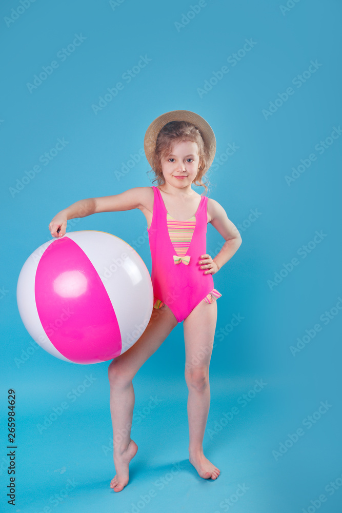 Little smiling girl in swimsuit with big inflatable ball on blue background Little smiling girl in swimsuit with big inflatable ball on blue background