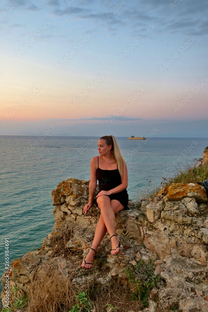 girl sits on a rock and looks at a beautiful view of the sea and sunset