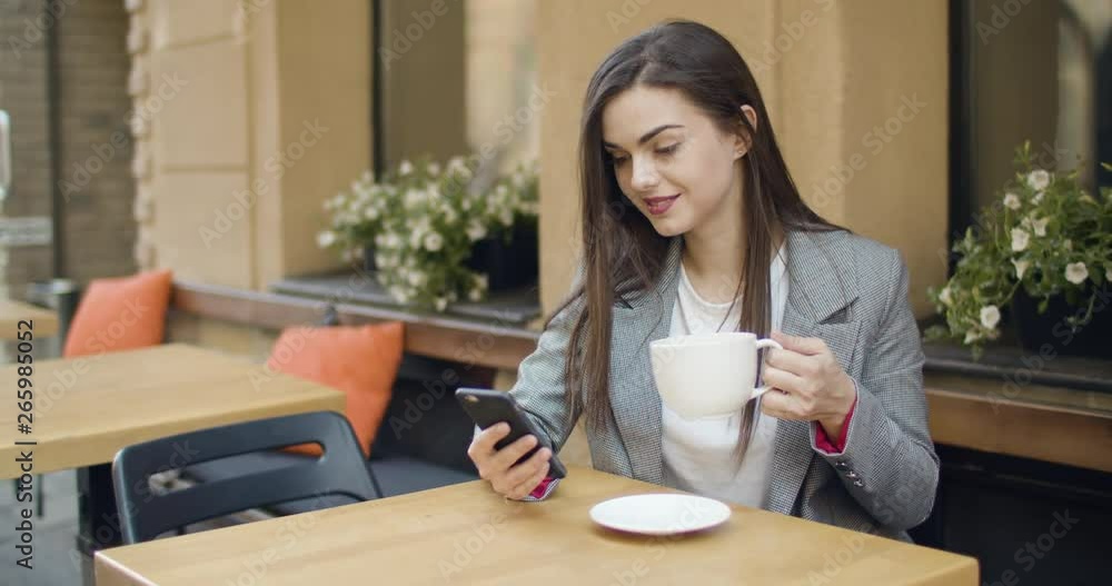 Beautiful young woman use smartphone for texting while drinking coffee in outdoors restaurant Beautiful young woman use smartphone for texting while drinking coffee in outdoors restaurant