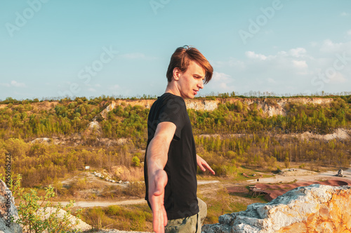 Handsome man is giving his hand in the mountains, while at the top of the cliff