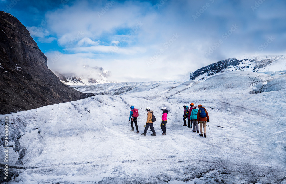 Back view of professional mountaineers in warm clothes walking on icy surface glacier by snowy mountain in Iceland