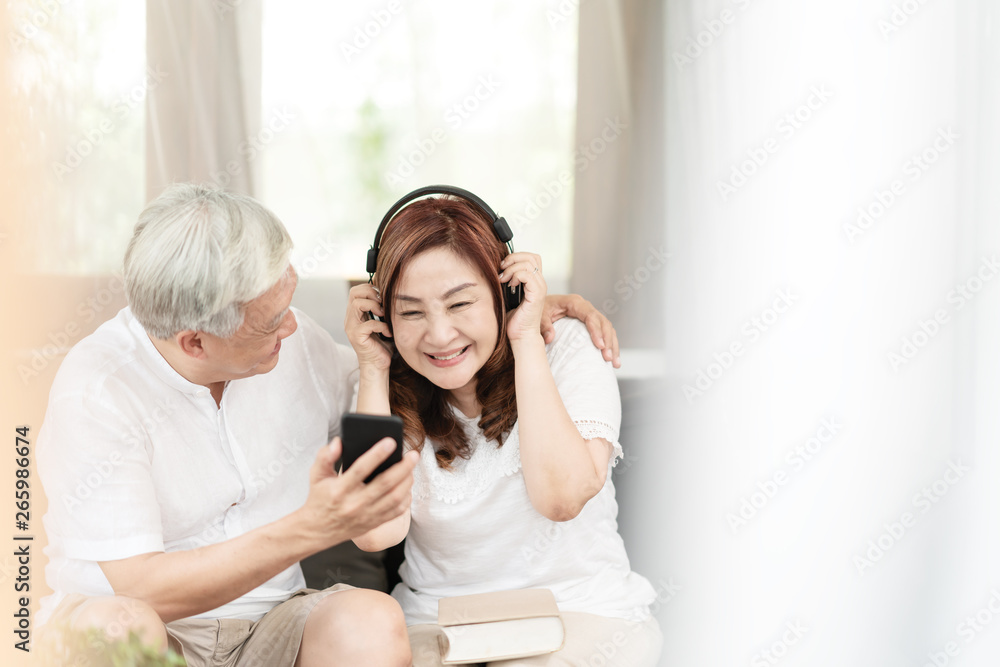 Candid of attractive older couple asian sitting relax together on couch at home in lifestyle of retirement people concept. Asian old man and senior woman listen to music on podcast from mobile phone. Candid of attractive older couple asian sitting relax together on couch at home in lifestyle of retirement people concept. Asian old man and senior woman listen to music on podcast from mobile phone.