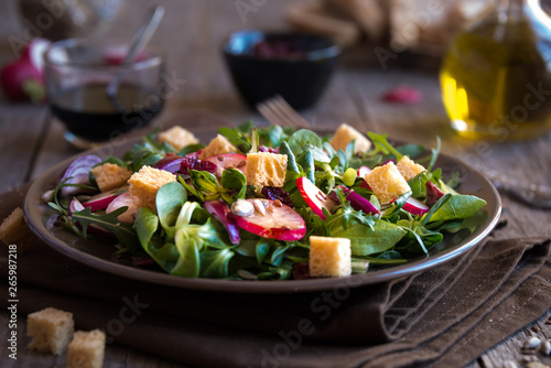 Fresh vegetable salad with radish, arugola, croutons on dark wood